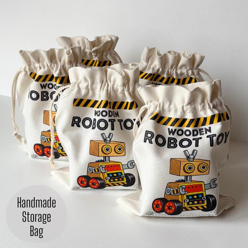 May include: A set of off-white canvas drawstring bags featuring a graphic of a yellow and red robot with the text WOODEN ROBOT TOY and a black and yellow hazard stripe pattern at the top. Each bag has a gathered top closure with matching drawstrings.