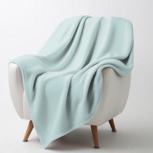 May include: A light blue blanket draped over a white armchair. The blanket is soft and plush, with visible folds and a smooth texture. The chair has wooden legs and a curved back, creating a cozy and inviting scene.