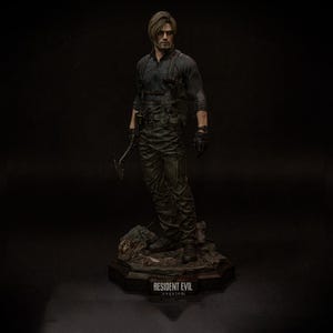 May include: A detailed figurine of a character from Resident Evil, dressed in a black tactical outfit and holding a weapon. The figure stands on a rocky base with the game's title, "Resident Evil Requiem," inscribed.