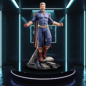 Könnte beinhalten: Detaillierte Statue eines Superhelden in dynamischer Pose, bekleidet mit einem blauen Anzug mit goldenen Akzenten und einem Umhang. Die Figur steht auf einem felsigen Sockel auf einer schwarzen Plattform, mit roten Stiefeln und leuchtend roten Augen.