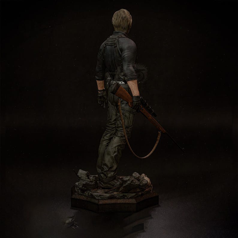 May include: A detailed figurine of a character in a black jacket and green pants, holding a rifle. The figure is standing on a textured base. The character is facing away from the viewer.