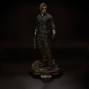 May include: A detailed figurine of a character from Resident Evil, dressed in a black tactical outfit and holding a gun. The figure stands on a rocky base with the text "RESIDENT EVIL requiem" at the bottom. The figure has short brown hair and is wearing black gloves.