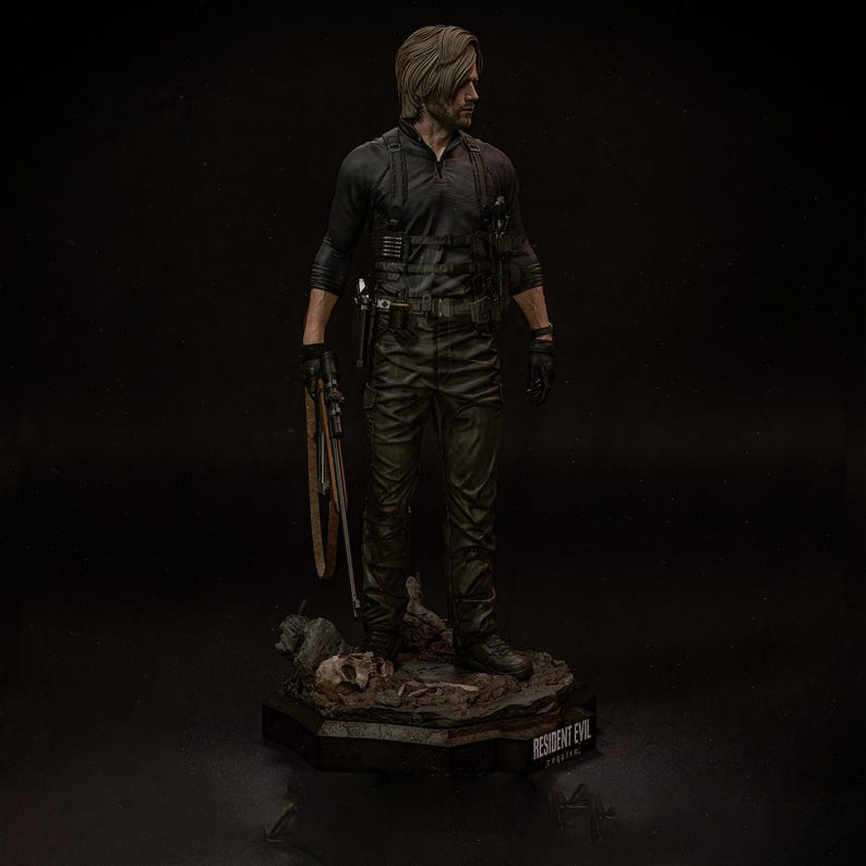 May include: A detailed figurine of a man in a black tactical outfit, holding a weapon. The figure stands on a base with the text "RESIDENT EVIL" and a skull. The figure has short, light brown hair and is looking to the side.