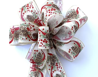 May include: A white ribbon with a gold trim and a pattern of pine cones, berries, and red ribbon. The ribbon is tied into a bow.