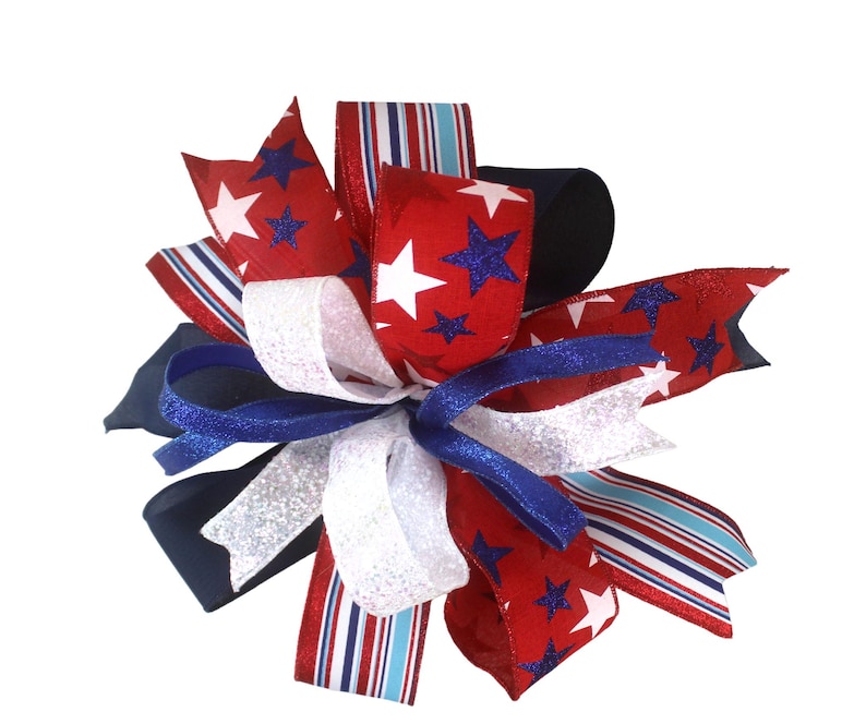 May include: A decorative bow featuring red, white, and blue ribbons. The red ribbons are adorned with white stars and blue glitter stars. White glitter and blue ribbons are also incorporated, creating a patriotic theme. The bow is suitable for various decorative purposes.