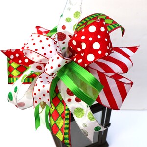 Pu&ograve; includere: Un topper per lanterna di Natale festivo con un grande fiocco fatto di nastro rosso, bianco e verde con pois e strisce.