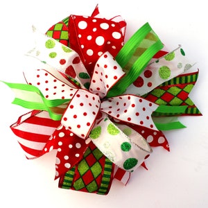 Pu&ograve; includere: Un fiocco di Natale realizzato con nastro rosso, bianco e verde. Il nastro presenta diversi motivi, tra cui pois, strisce e un motivo a quadri.