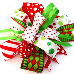 Pu&ograve; includere: Un fiocco di Natale realizzato con nastro rosso, bianco e verde. Il fiocco presenta pois, strisce e un motivo a rombi.