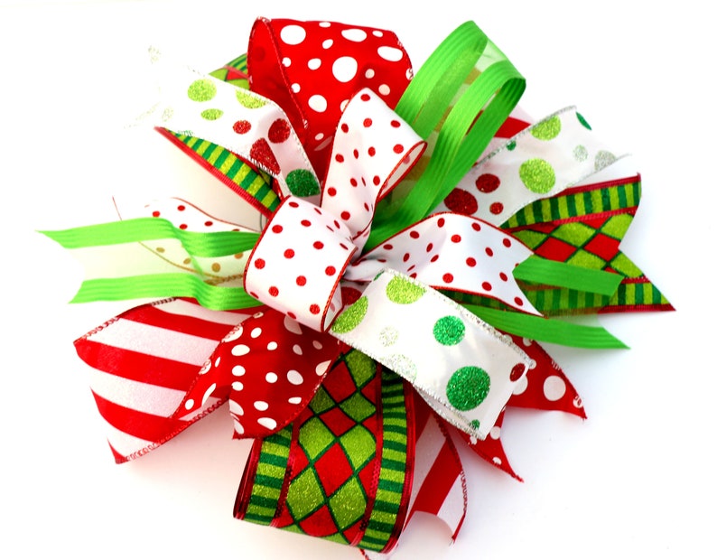 Pu&ograve; includere: Un fiocco di Natale realizzato con nastro rosso, bianco e verde. Il fiocco presenta pois, strisce e un motivo a rombi.