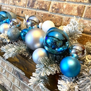 May include: A silver and blue Christmas garland with ornaments and frosted pine branches.