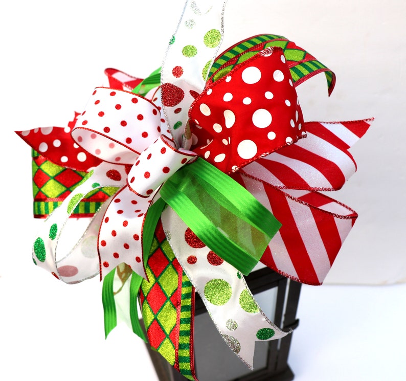 Pu&ograve; includere: Un topper per lanterna di Natale festivo con un grande fiocco fatto di nastro rosso, bianco e verde con pois e strisce.
