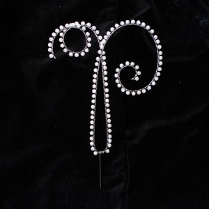 May include: A white pearl cake topper shaped like the letter 'P' with a wire frame.