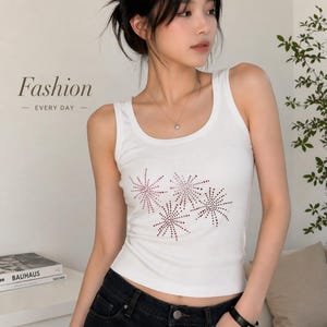 May include: White vest top with a scoop neck and a sparkly, starburst design. The text "Fashion EVERY DAY" is displayed on the left side of the image. The model is wearing black jeans and a black bracelet.