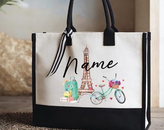May include: A canvas tote bag with black handles and trim. The bag features a watercolor design of the Eiffel Tower, a bicycle with a basket of flowers, and a suitcase. The word "Name" is written in script.