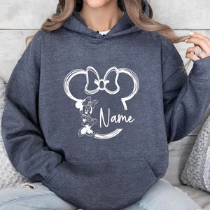 K&ouml;nnte beinhalten: Ein dunkelblauer Kapuzenpullover mit einer wei&szlig;en Umrandung von Minnie Mauss Kopf und Schleife und dem Wort "Name" darunter.