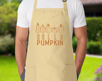 May include: A beige apron featuring a graphic of five orange line-art pumpkins arranged in a row above the text "HELLO PUMPKIN" in orange lettering. The apron includes an adjustable neck strap with a black buckle and two front pockets.
