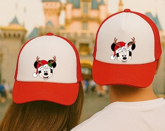 May include: Two red and white baseball caps with a Mickey Mouse graphic wearing a Santa hat and reindeer antlers. The caps have a red brim and mesh back. The background shows a castle.
