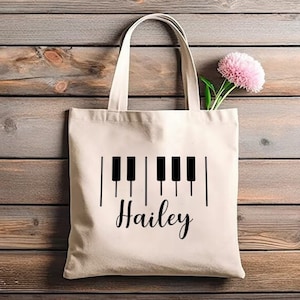 May include: A white canvas tote bag with black piano keys and the name "Hailey" printed on it.