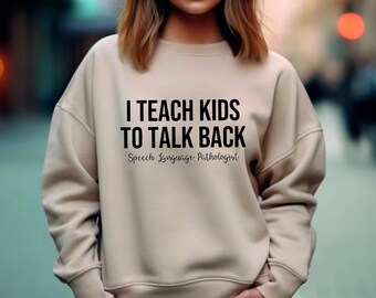 May include: A beige sweatshirt with the text "I teach kids to talk back" and "Speech Language Pathologist" printed on the front.