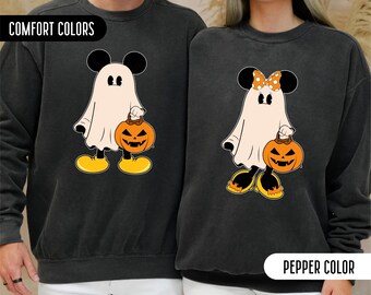 May include: Two charcoal gray crewneck sweatshirts featuring graphic prints of ghosts dressed as Mickey and Minnie Mouse. Each ghost wears a white sheet, yellow shoes, and carries an orange jack-o'-lantern bucket. The Minnie ghost has an orange polka-dot bow.