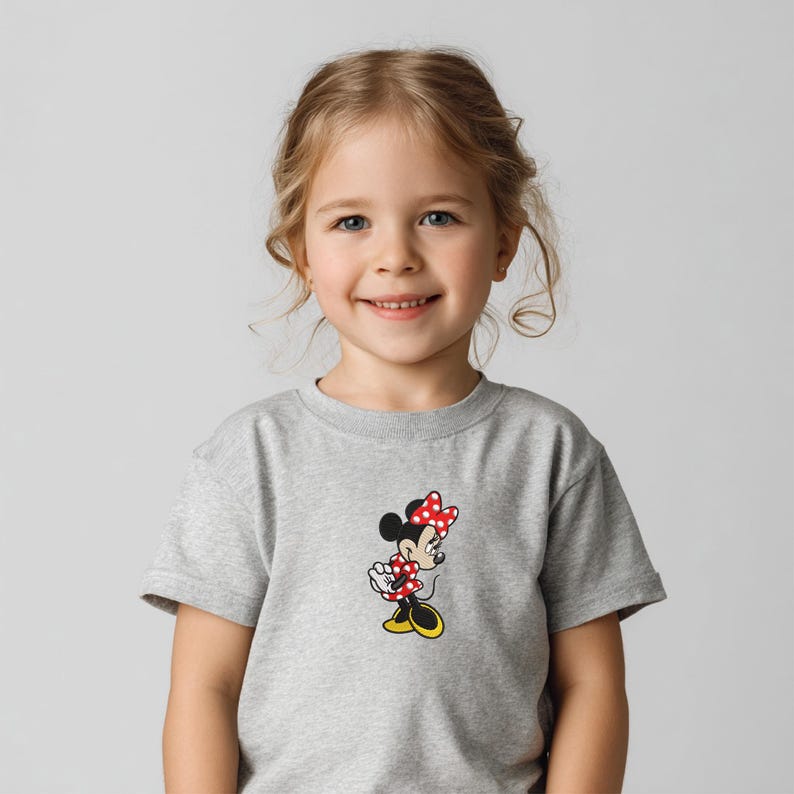 May include: A gray t-shirt featuring a Minnie Mouse graphic. The cartoon character is depicted in a classic pose, wearing a red polka-dot bow and dress. The shirt is made of a soft, comfortable material.