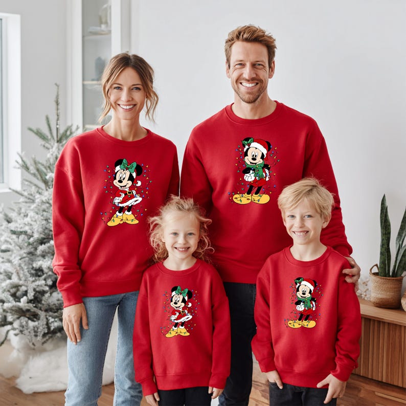 K&ouml;nnte beinhalten: Rote Sweatshirts mit einem Weihnachtsdesign von Minnie Mouse und Mickey Mouse. Die Sweatshirts werden von einer vierk&ouml;pfigen Familie getragen. Das Minnie Mouse-Design hat eine gr&uuml;ne Schleife und gelbe Schuhe. Das Mickey Mouse-Design hat einen Weihnachtsmannhut und einen gr&uuml;nen Schal.