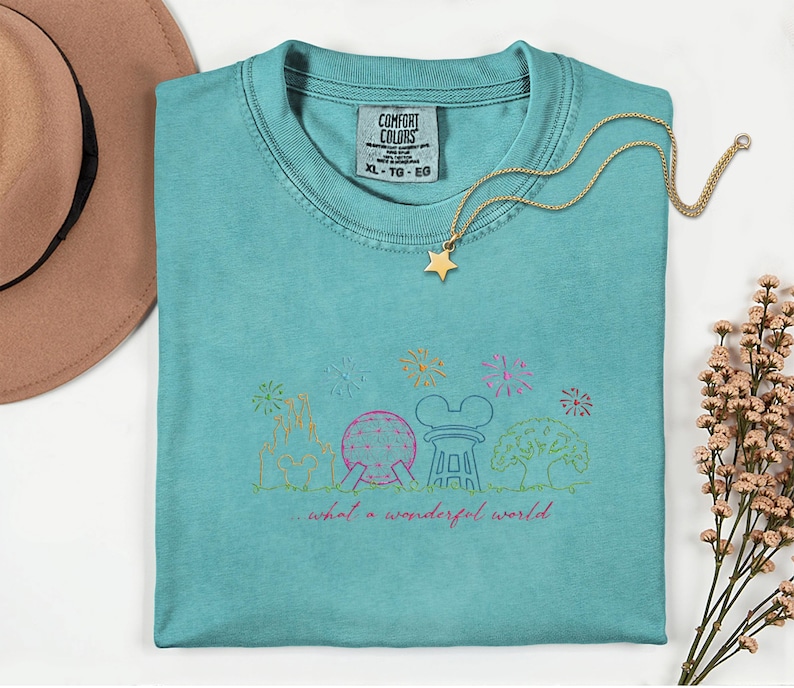 May include: A turquoise Comfort Colors XL t-shirt with a gold star necklace. The shirt features a colorful line drawing of a theme park with fireworks and the text "...what a wonderful world."