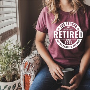May include: A maroon t-shirt with a white circle graphic that says "The Legend Has Officially Retired Since 2025 Not My Problem Anymore".