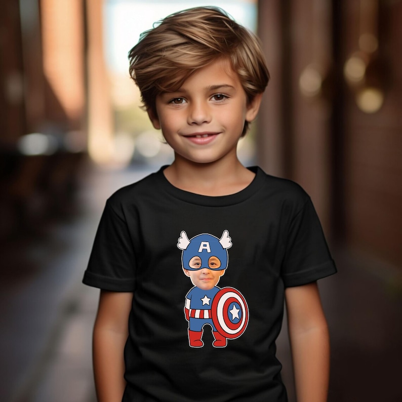 K&ouml;nnte beinhalten: Ein kleiner Junge tr&auml;gt ein schwarzes T-Shirt mit einem Comicbild von Captain America. Die Comicfigur hat das Gesicht des Jungen dar&uuml;bergelegt. Die Comicfigur tr&auml;gt ein blaues und rotes Kost&uuml;m mit einem rot-wei&szlig;-blauen Schild.