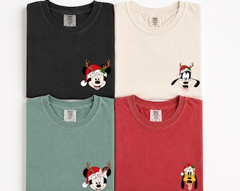 May include: Four t-shirts in black, cream, sage green, and red. Each shirt features a small graphic on the chest of a Disney character wearing a Santa hat with reindeer antlers. The characters include Mickey Mouse, Goofy, Minnie Mouse, and Pluto.