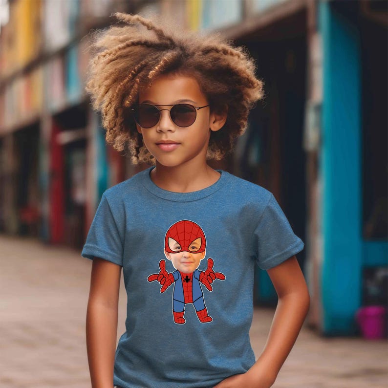 K&ouml;nnte beinhalten: Ein junges Kind tr&auml;gt ein blaues T-Shirt mit einem Comicbild von Spider-Man, auf dem das Gesicht des Kindes auf das Gesicht des Charakters gelegt wurde. Das Kind tr&auml;gt eine Sonnenbrille und hat lockiges braunes Haar.