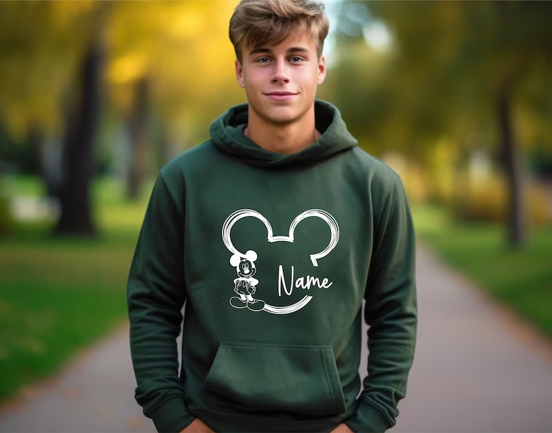 K&ouml;nnte beinhalten: Ein dunkelgr&uuml;ner Kapuzenpullover mit einer wei&szlig;en Umrandung von Mickey Mouse' Kopf und dem Wort "Name" darunter.