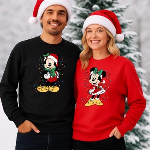 K&ouml;nnte beinhalten: Passende schwarze und rote Weihnachtspullover mit Mickey und Minnie Mouse. Mickey tr&auml;gt einen Weihnachtsmannhut und einen Schal, umgeben von Lichtern. Minnie tr&auml;gt ein Kleid und eine Schleife, ebenfalls mit Lichtern. Beide tragen gelbe Schuhe. Das Paar im Bild tr&auml;gt Weihnachtsm&uuml;tzen.