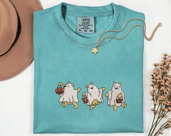 May include: A teal short-sleeve t-shirt with a crew neckline and a Comfort Colors label. The shirt features an embroidered graphic of three yellow bears wearing white ghost costumes and carrying orange jack-o'-lantern trick-or-treat buckets.