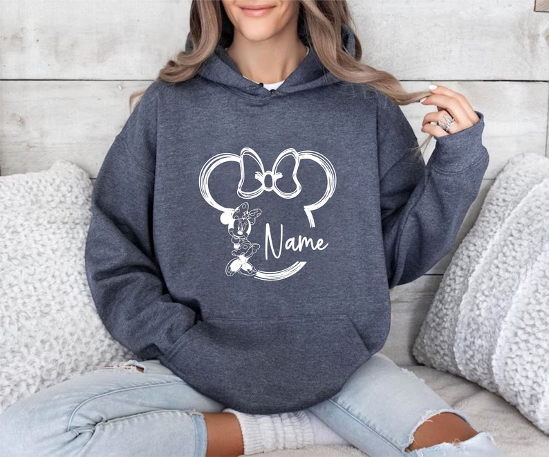 K&ouml;nnte beinhalten: Ein dunkelblauer Kapuzenpullover mit einer wei&szlig;en Umrandung von Minnie Mauss Kopf und Schleife und dem Wort "Name" darunter.