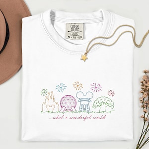 May include: White Comfort Colors t-shirt with a colorful line drawing of a castle, sphere, and other theme park icons. The text "...what a wonderful world" is below the drawing. A gold star necklace is on the shirt.