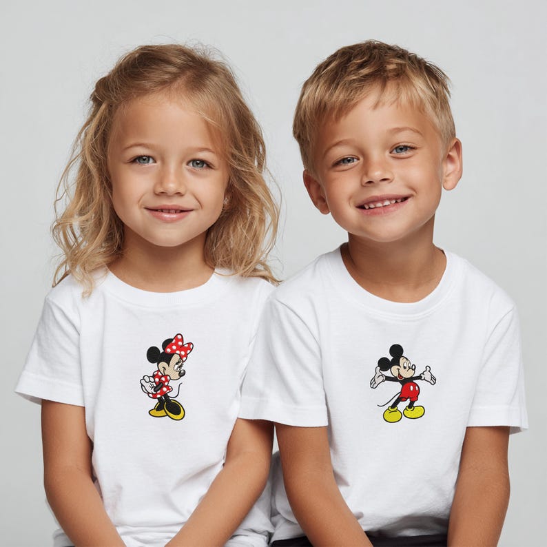 May include: Two children wearing white t-shirts with cartoon character designs. One shirt features Minnie Mouse in a red polka-dot bow and dress. The other shirt displays Mickey Mouse in red shorts and yellow shoes. Both shirts are short-sleeved.