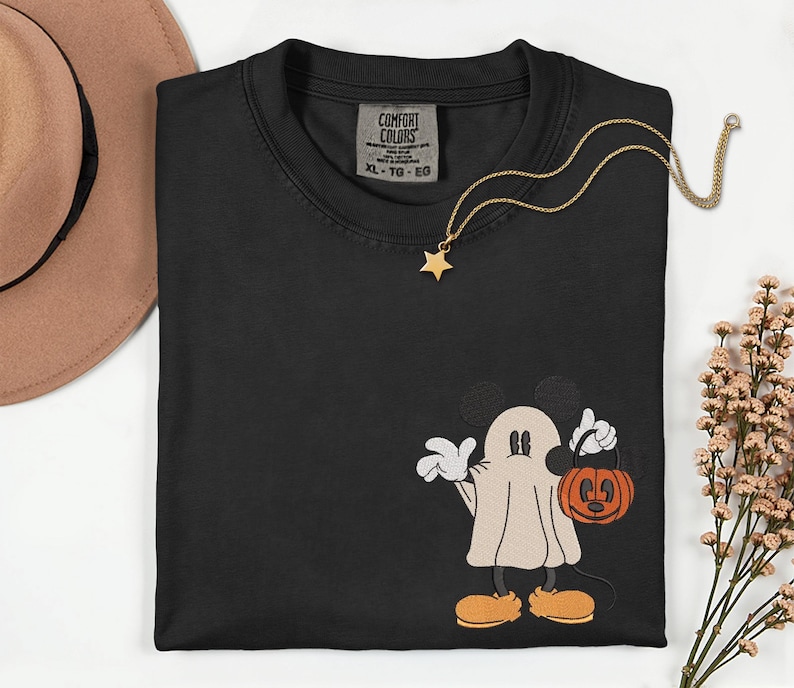 Pu&ograve; includere: T-shirt nero Comfort Colors con un design di Mickey Mouse fantasma a tema Halloween. La grafica ricamata presenta Mickey in costume da fantasma che tiene in mano un secchio a forma di zucca. Una collana con pendente a stella dorata &egrave; drappeggiata sulla maglietta.