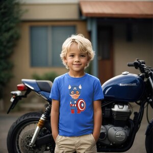 K&ouml;nnte beinhalten: Ein kleiner Junge tr&auml;gt ein blaues T-Shirt mit einem Comicbild von Captain America. Das Bild zeigt das Gesicht des Jungen auf dem Kopf des Charakters. Der Junge steht vor einem Motorrad.
