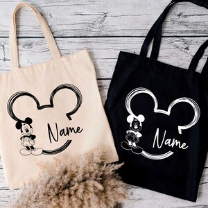 May include: Two tote bags with a black and white Mickey Mouse design. One bag is black with white text and the other is white with black text. Both bags have the word "Name" printed on them.