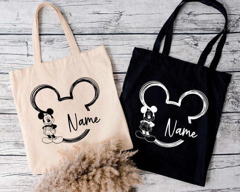 May include: Two tote bags with a black and white Mickey Mouse design. One bag is black with white text and the other is white with black text. Both bags have the word "Name" printed on them.