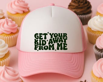 May include: A pink and white trucker hat with the text "GET YOUR KID AWAY FROM ME" in green. The hat is surrounded by cupcakes with pink and chocolate frosting.