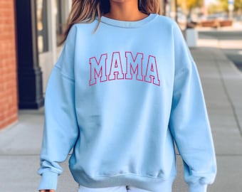 May include: A light blue sweatshirt with the word "MAMA" printed in pink on the front. The sweatshirt has a relaxed fit and a crew neck.
