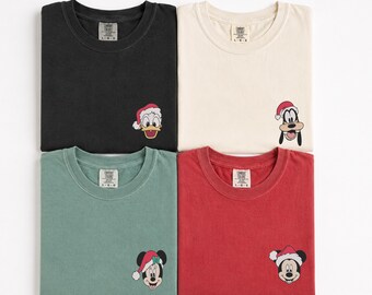 May include: Four short-sleeve t-shirts in black, cream, sage green, and red. Each shirt features a small embroidered graphic of a Disney character wearing a Santa hat: Donald Duck, Goofy, Minnie Mouse, and Mickey Mouse. Each has a Comfort Colors label.