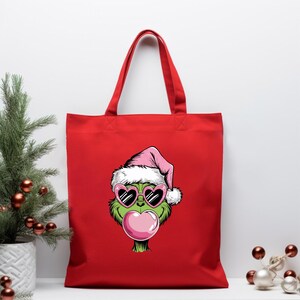 May include: Red tote bag featuring a cartoon Grinch character wearing a pink Santa hat and heart-shaped sunglasses, blowing a bubblegum bubble. The bag has a simple design with a solid red color and sturdy handles.
