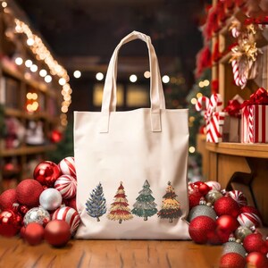 May include: Cream-colored tote bag featuring five illustrated Christmas trees in blue, red, green, and yellow. The bag has two handles and is surrounded by red and silver Christmas ornaments, and candy canes.