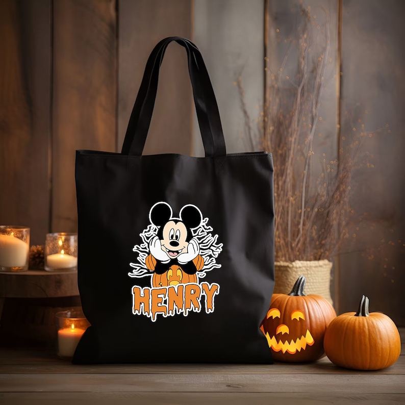 May include: Black canvas tote bag with a Mickey Mouse character dressed as a pumpkin. The bag has the name "HENRY" printed in orange dripping letters.