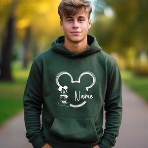 K&ouml;nnte beinhalten: Ein dunkelgr&uuml;ner Kapuzenpullover mit einer wei&szlig;en Umrandung von Mickey Mouse' Kopf und dem Wort "Name" darunter.