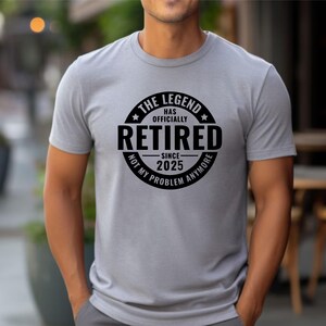 May include: A grey t-shirt with a black circle graphic that says "The Legend Has Officially Retired - Since 2025 - Not My Problem Anymore".