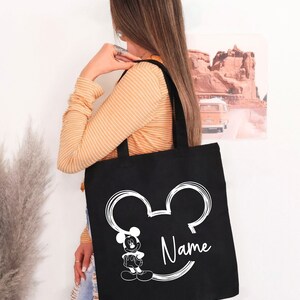 May include: Black tote bag with a white outline of Mickey Mouse's ears and a white image of Mickey Mouse inside the ears. The text "Name" is written in white cursive below the image.